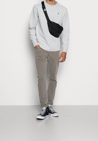 Chemise à manches longues gris clair, pantalon slim beige, sac crossbody noir et baskets montantes noires avec semelles et lacets blancs.