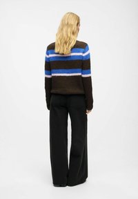 Brown striped sweater with blue, pink, and black horizontal lines; soft, textured fabric; worn with black wide-leg pants.