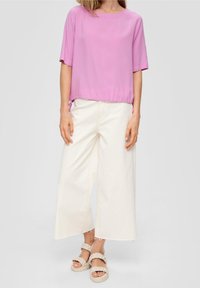 Haut rose à manches courtes avec un ourlet froncé, associé à un pantalon blanc à jambes larges et des sandales tressées légères. Tissu lisse avec une coupe décontractée.