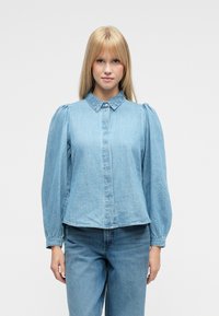 Jasnoniebieska koszula dżinsowa z bufkami na rękawach, spiczastym kołnierzem i zapięciem na guziki z przodu. Gładka tekstura, luźny krój.