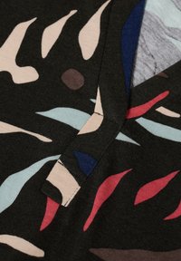 Tissu multicolore présentant des motifs abstraits de feuilles dans des nuances de rouge, bleu, rose et tons terreux sur un fond noir. Texture douce.