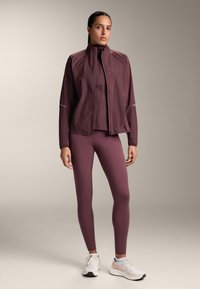 Bordeauxkleurige lichte jas met een hoge kraag, gecombineerd met bijpassende legging. Reflecterende accenten, gladde textuur en een getailleerd ontwerp.