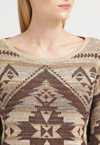 Brun och beige mönstrad tröja med vid halsringning, med geometriska mönster och en strukturerad stickad tyg.