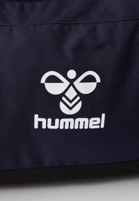 Hvit stilisert bie-logo og "hummel" tekst på mørkeblått stoff, sannsynligvis en del av en bag eller klesplagg.