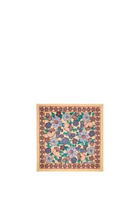 Pañuelo cuadrado con un patrón floral que presenta flores azules, blancas y marrones sobre un fondo beige, bordeado con un borde rojo oscuro. Acabado texturizado.