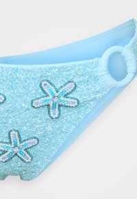 Gaiši zila peldbikses apakšdaļa ar teksturētām pērlēm, ar ziedu rotājumiem zilos un baltos toņos, kā arī sānu gredzena detaļu.