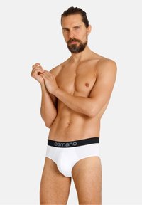 Weiße Baumwollslips mit einem schwarzen elastischen Bund, der mit einem grauen Logo versehen ist. Das Design ist enganliegend mit einer glatten Textur und minimalen Nähten.