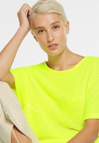 Neon-gelbes gestricktes Sweatshirt mit lockerer Passform und weitem Ausschnitt. Die Textur ist nätzig und hat kurze Ärmel.