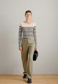 Top de mangas longas com riscas pretas e creme, calças verde-azeitona de cintura alta, mala preta e sapatos pretos; design minimalista, textura suave.