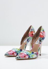 Escarpins floraux à talons hauts avec des pointes effilées, présentant un motif multicolore de fleurs et des accents de motif animal, sur un talon aiguille blanc.