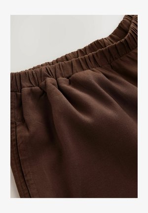 Pantaloni di stoffa marrone con cintura elastica, caratterizzati da una texture liscia e pieghe sottili per un volume aggiuntivo. Nessun motivo o accento visibile.