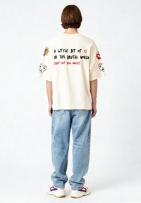 Krēmkrāsas pārmērīgi liels T-krekls ar grafiskiem tekstiem un ilustrācijām uz aizmugures. Saskaņots ar gaiši ziliem džinsiem un baltām kedām.