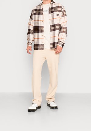 Ruudullinen paita beige, ruskea ja oranssi; valkoinen T-paita alla; kermaisen väriset housut; valkoiset kengät mustilla pohjilla; rento malli.