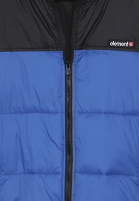 Gilet matelassé bleu avec une partie supérieure noire, doté d'une fermeture éclair à l'avant, du logo de la marque "element" sur le côté gauche, et d'une texture lisse.