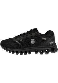 Scarpa da ginnastica nera realizzata in mesh e materiali sintetici, dotata di una suola testurizzata con ritagli circolari e un piccolo logo sul lato.