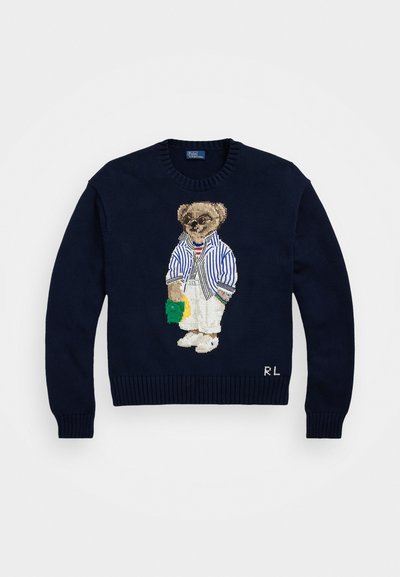 Pulôver de malha azul-marinho com um urso bordado que usa uma camisa às riscas, calças brancas e óculos de sol, com detalhes em verde e amarelo.