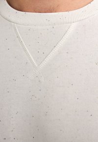 Light cream sweatshirt fabric with a textured ribbed collar, featuring scattered dark and blue speckles, and a V-shaped stitching detail.