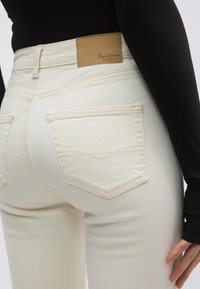 Άσπρο τζιν παντελόνι από ντένιμ με λεία υφή, ψηλή μέση, ορατές πίσω τσέπες και δερμάτινο ταμπελάκι σε ταμπά απόχρωση με την ετικέτα "Pepe Jeans London".