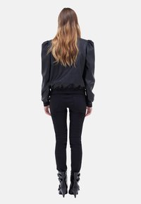 Svart läder bomberjacka med puffade axlar, åtsittande midja och ribbade ärmslut, tillsammans med svarta skinny jeans och klackade ankelstövlar.