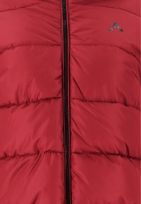 Röd vadderad väst med quiltade sektioner, svart dragkedja och diskret varumärke. Materialet verkar lätt och vattenavvisande med en slät textur.