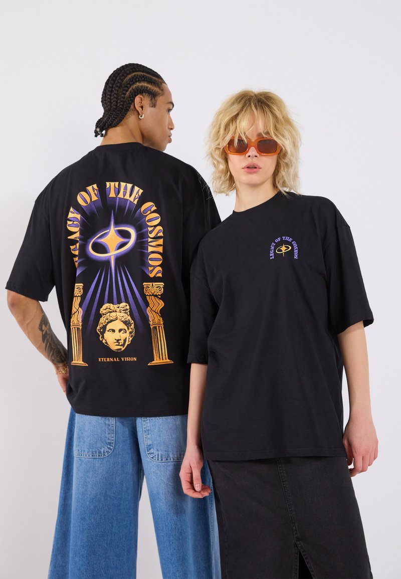 Black oversized t-shirts with bold graphic prints. One features a colorful cosmic design on the back; the other has a small chest print.