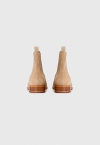 Botas de tobillo de ante beige con un acabado mate, que presentan una puntera redonda, un diseño minimalista y un tacón bajo de madera. Panel lateral elástico para facilitar su uso.