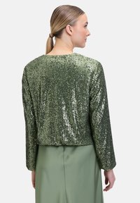 Grüne Paillettenjacke mit Rundhalsausschnitt und langen Ärmeln, die eine glänzende Textur und ein kurzes Design aufweist, kombiniert mit einem passenden Rock.