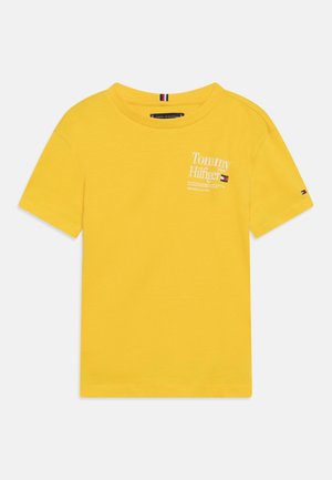 Żółta koszulka z krótkim rękawem i okrągłym dekoltem, z białym napisem logo Tommy Hilfiger i małą flagą na piersi i rękawie.