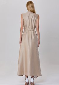 Robe maxi en satin beige avec un design sans manches, taille élastique, texture douce et silhouette fluide. Présente un détail dans le dos et un ourlet en couches.