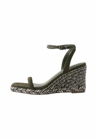 Sandalo a cuneo verde oliva con una fascia anteriore bassa, cinturino alla caviglia e base intrecciata con motivo a spina di pesce. Materiale scamosciato con una texture liscia.