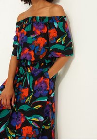 Robe florale décolletée en tissu noir avec des motifs vifs rouges, violets et verts ; taille smockée et poches latérales.