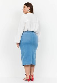 Svetlo modra denim krilo v obliko svinčnika z režo na hrbtni strani, visok pas in gladka tekstura, v kombinaciji z belo bluzo in rdečimi blok peta sandalami.