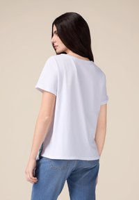 Tricou alb din bumbac, cu mânecă scurtă, guler rotund și o croială lejeră. Purtați cu blugi albaștri, prezentând un design simplu și minimalist.