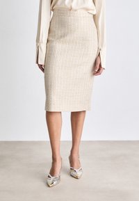 Beige vævet pencil skirt med struktureret m�ønster, høj talje og knælængde. Parret med metalliske to-tonede hæle med spids tå.