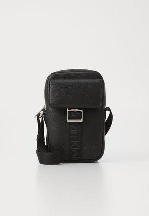 Bolsa de ombro em pele negra com superfície texturizada, aba frontal, hardware prateado e logotipo em relevo na alça. Formato retangular compacto.