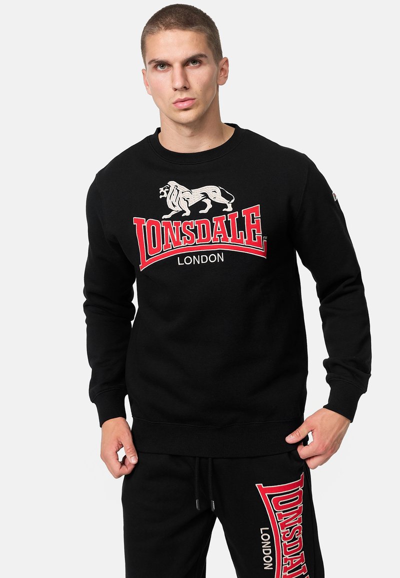 Felpa nera in cotone con polsini a costine, caratterizzata da un grande logo Lonsdale bianco e rosso e da una grafica di un leone sulla parte anteriore.