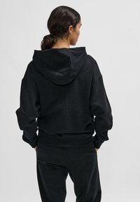 Czarna krótka bluza z kapturem na sznurku, szerokimi rękawami i miękką fakturą, w połączeniu z dopasowanymi czarnymi spodniami.
