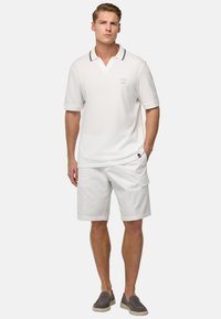 Chemise polo blanche avec décolleté en V et accents de col gris, associée à un short blanc et des chaussures slip-on grises, présentant un détail de logo sur la poitrine.