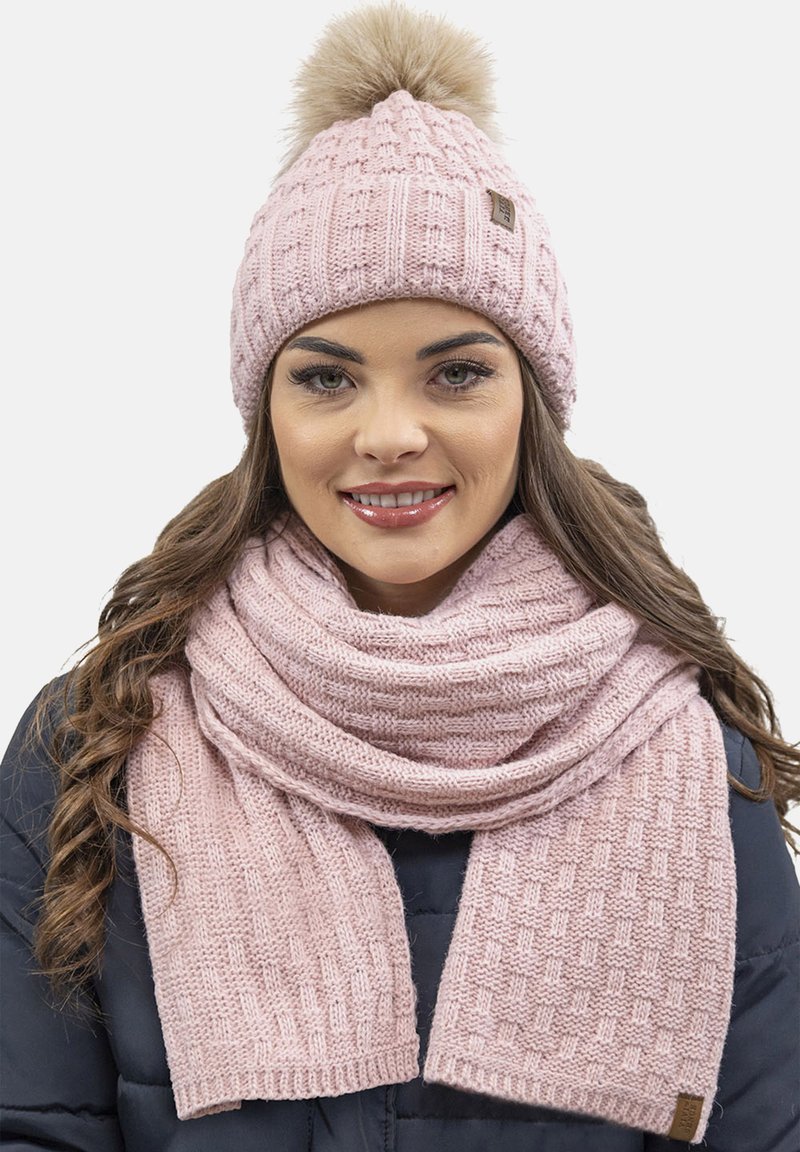 Gorro de punto rosa con un pompón de pelo sintético y una bufanda texturizada a juego. Ambos artículos presentan un patrón de bloques y un hilo suave y grueso.