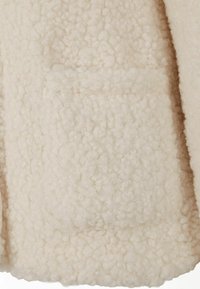 Kremo spalvos vilna audinys su tekstūruotu, pūkuotu paviršiumi. Yra kišenė ir minkšta, jauki išvaizda.