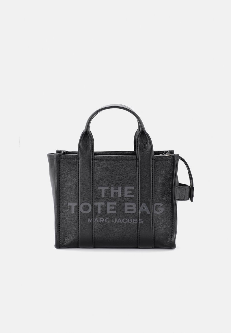 Crna kožna torba s dvostrukim gornjim ručkama, strukturnog oblika, s utisnutim tekstom "THE TOTE BAG" i "MARC JACOBS" sprijeda. Uključeni su podesivi remen.