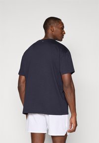 Σκούρο μπλε βαμβακερή μπλούζα με κοντό μανίκι και στρογγυλή λαιμόκοψη. Διαθέτει ένα μικρό λογότυπο στη πίσω πλευρά του λαιμού και έχει άνετη εφαρμογή.