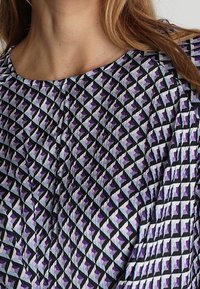 Mönstrad blus med en diamantdesign i lila, svart och ljusblått, med rund halsringning och subtilt strukturerad yta.