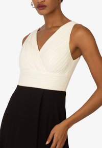 Ärmelloses Kleid mit einem gefältelten weißen Oberteil und einem einfarbigen schwarzen Rock, mit einer figurbetonten Taille und einem V-Ausschnitt.