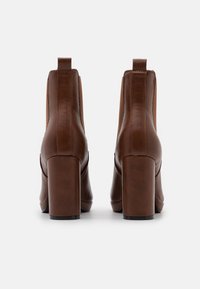 Stivali alla caviglia in pelle marrone con punta rotonda, tacco a blocco e pannelli laterali in elastico. Presentano una texture liscia e un design minimalista.