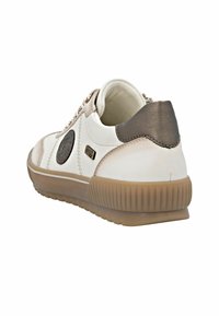 Bílé a béžové tenisky s texturovaným povrchem, kruhovým logem a hnědým akcentem na patě. Gumová podrážka s vroubkovaným okrajem.