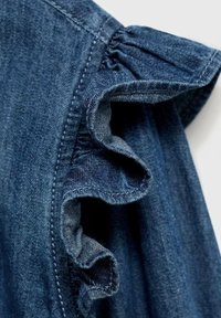 Denimbeklædning med design af flagrende ærmer og samlede detaljer. Stoffet er en mørkeblå, tekstureret vævning med synlig syning.