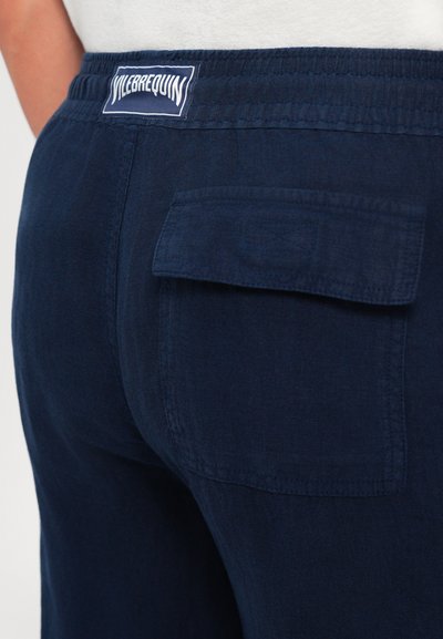 Nahaufnahme von marineblauen Hosen mit elastischem Bund und Klappentasche, ausgestattet mit einem weißen Vilebrequin-Logo-Patch.