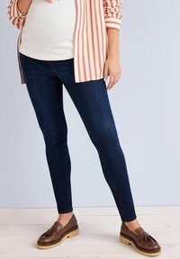 Tummansiniset farkut slim fit -mallia, yhdistettynä raidalliseen korallinväriseen ja valkoiseen nappipaitaan sekä ruskeisiin loafer-kenkiin, joissa on vaaleanruskea pohja.
