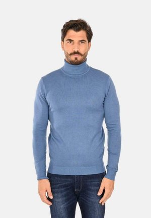 Maglione a collo alto blu realizzato in materiale morbido, con un design aderente, dettagli a coste al colletto e all'orlo, indossato con jeans scuri.